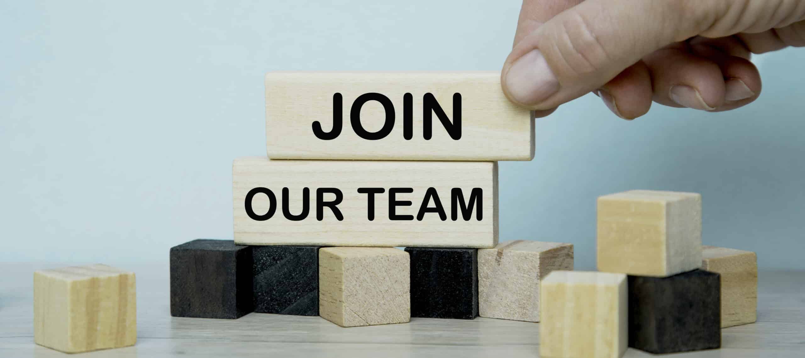 Text JOIN OUR TEAM writing in cubes. CUBE in hand on a blue background. Business concept